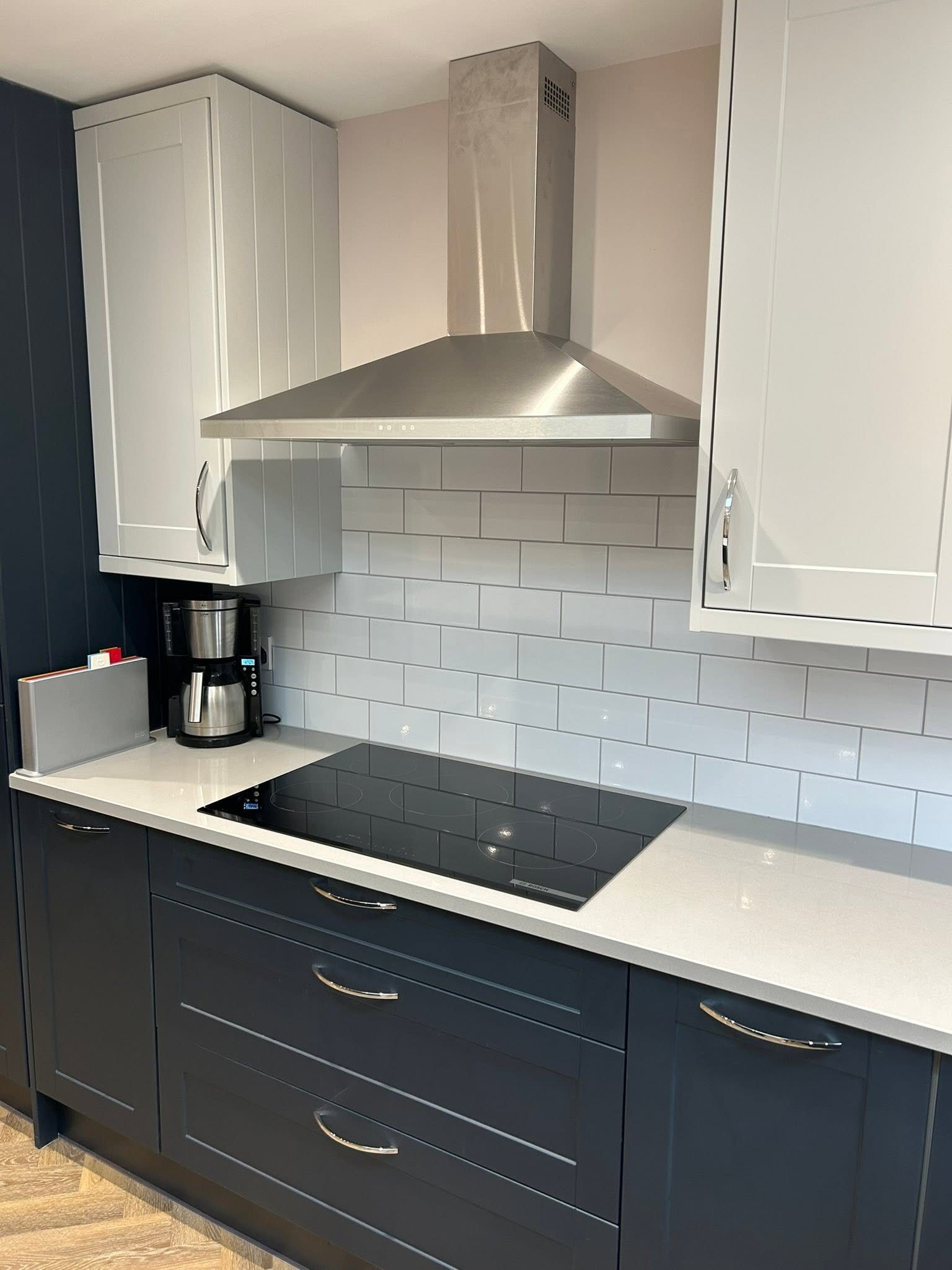 Kitchen with white wall cabinets, navy base cabinets and a tiled splashback